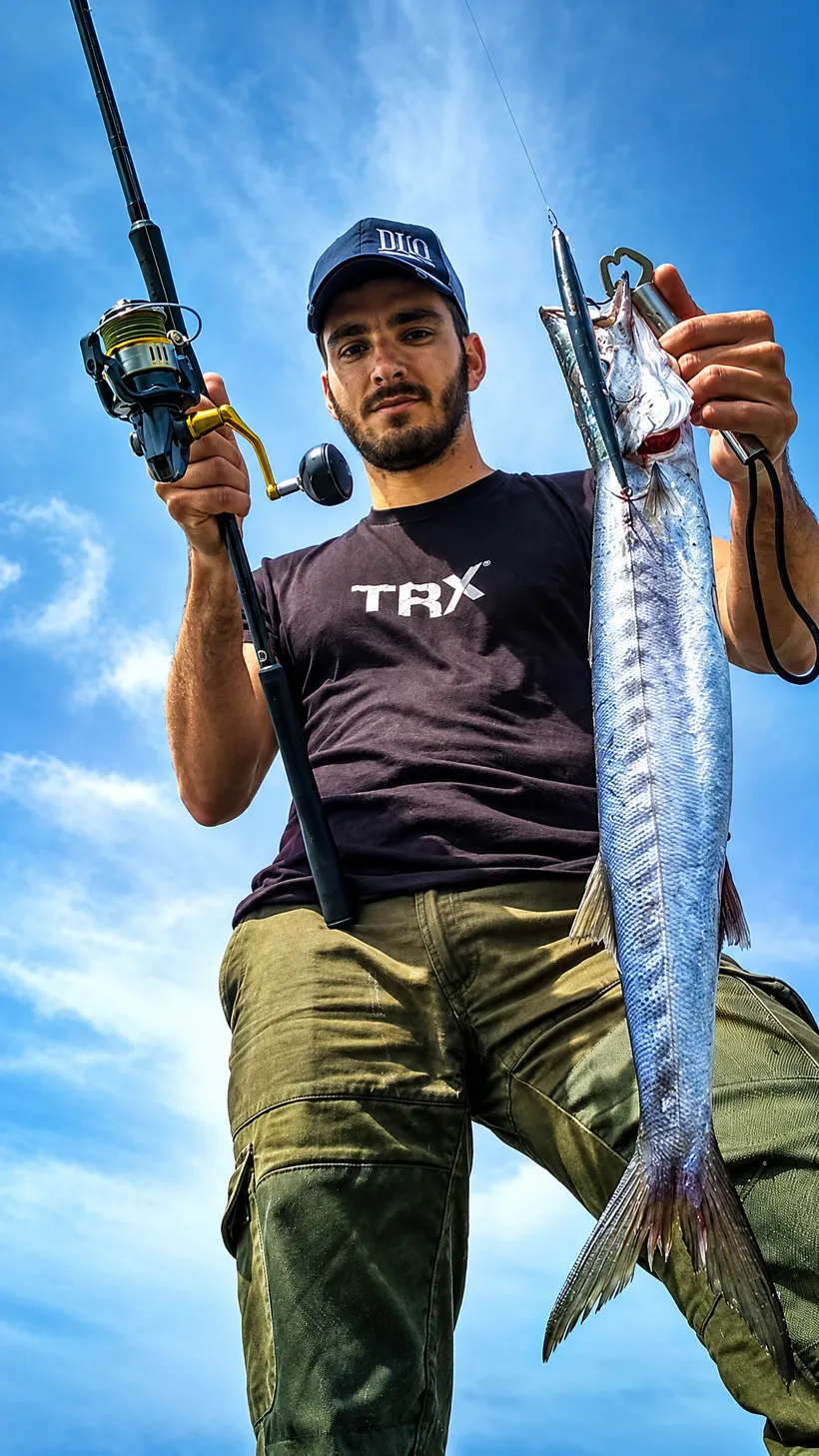Action Team angler holding a barracuda and a spinning rod against a blue sky