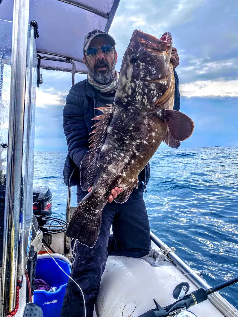 Angler on a small boat holding a large grouper