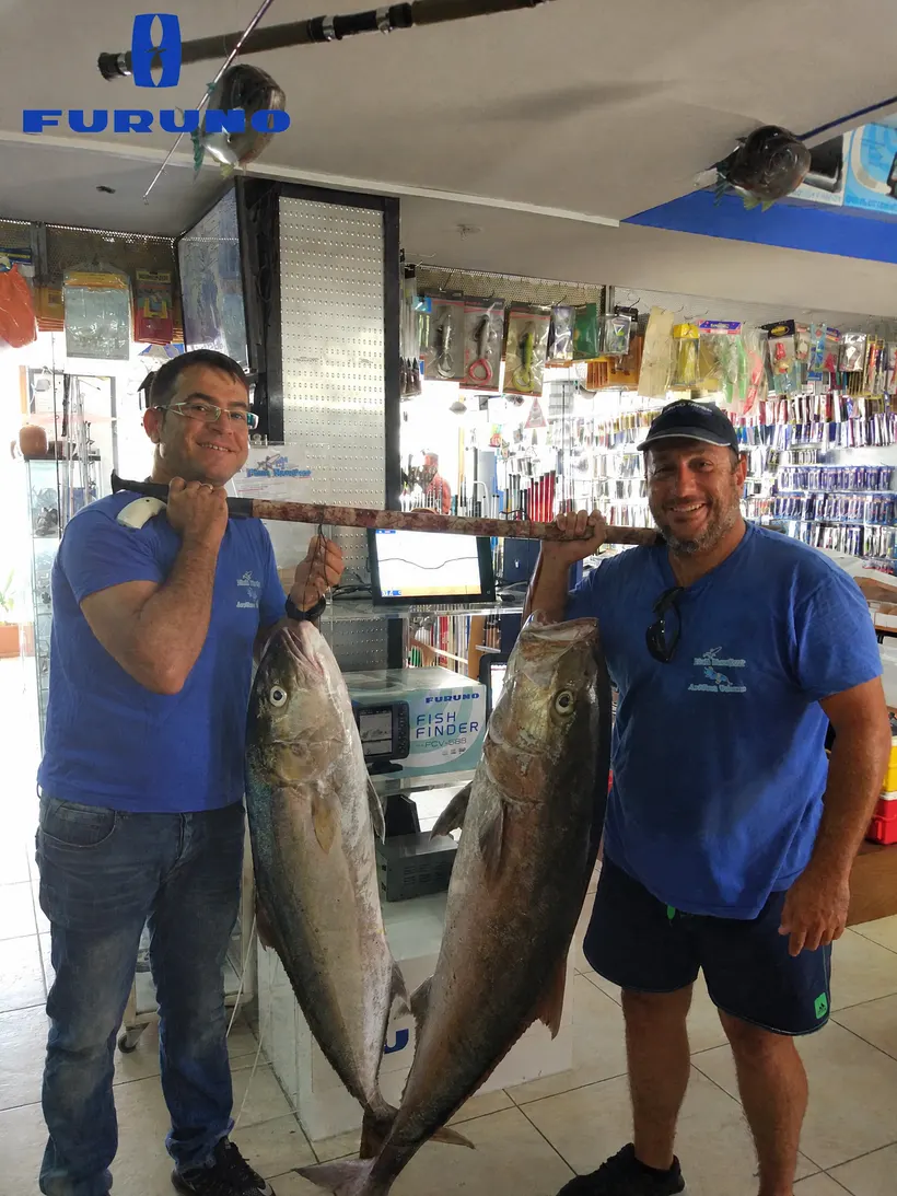 Two Fish Hunter team members inside the shop carrying two big fish on a pole